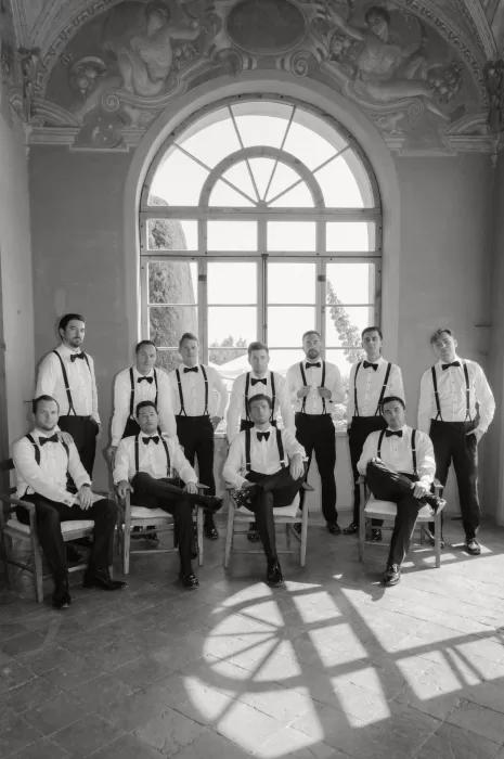 Groomsmen gather inside Villa San Vigilio in a dramatic black and white portrait with classic arched windows and painted ceilings.
