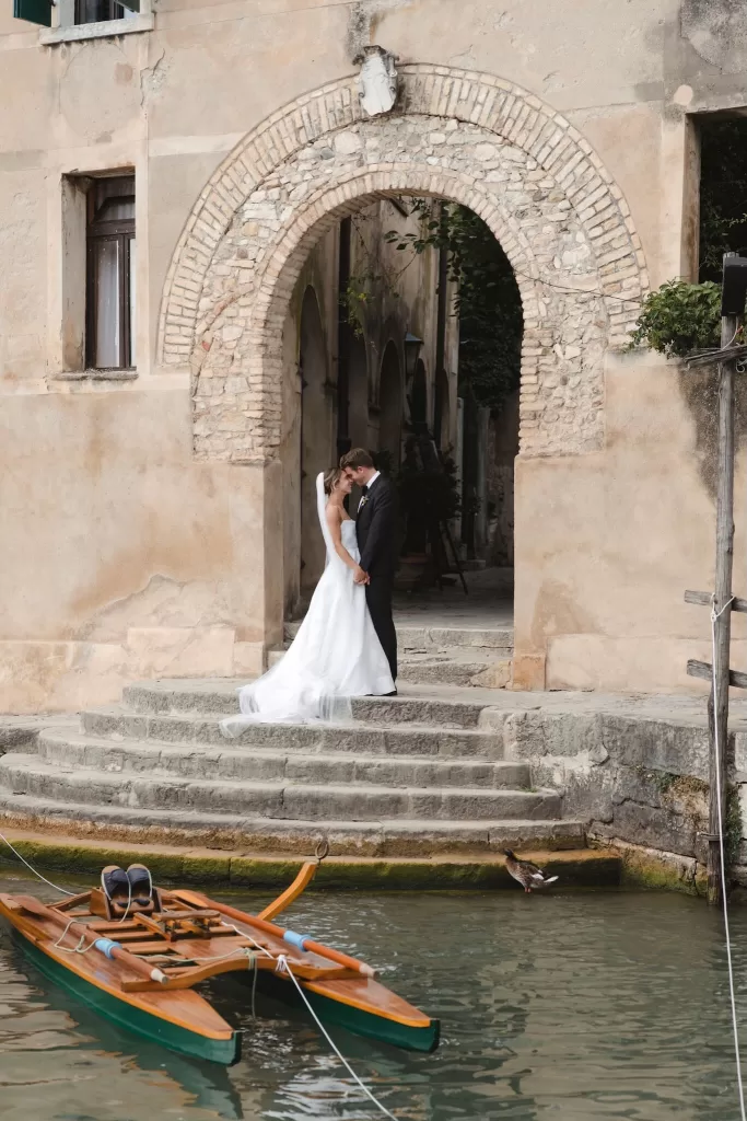 Romantic kiss under a historic stone archway at Villa San Vigilio, with the couple framed on ancient steps by the water.