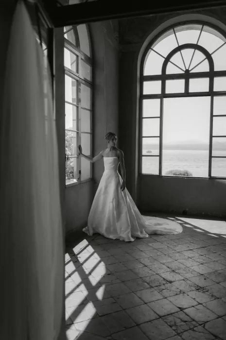 Bride gazes out the window of Villa San Vigilio in elegant black and white, framed by soft natural light and lake views.