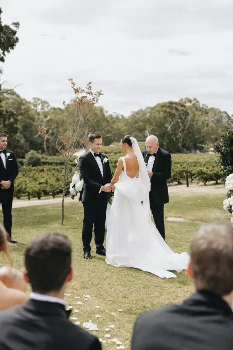 Bride and groom holding hands during vineyard ceremony, surrounded by greenery at Le Mas Barossa.