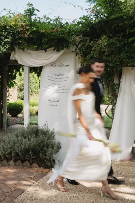 Blurred motion photo of the bride and groom walking past their wedding menu backdrop at Wallalong House.