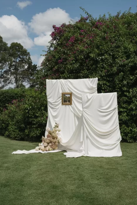 White draped fabric backdrop with florals and framed painting set on the lawn at Wallalong House.