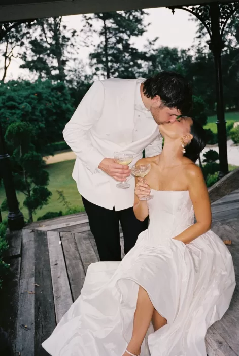 Bride and groom toasting with champagne glasses and sharing a kiss at their Wallalong House reception.