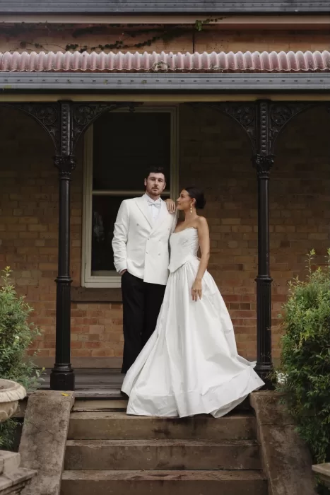 Bride and groom standing arm in arm on the veranda steps of Wallalong House.