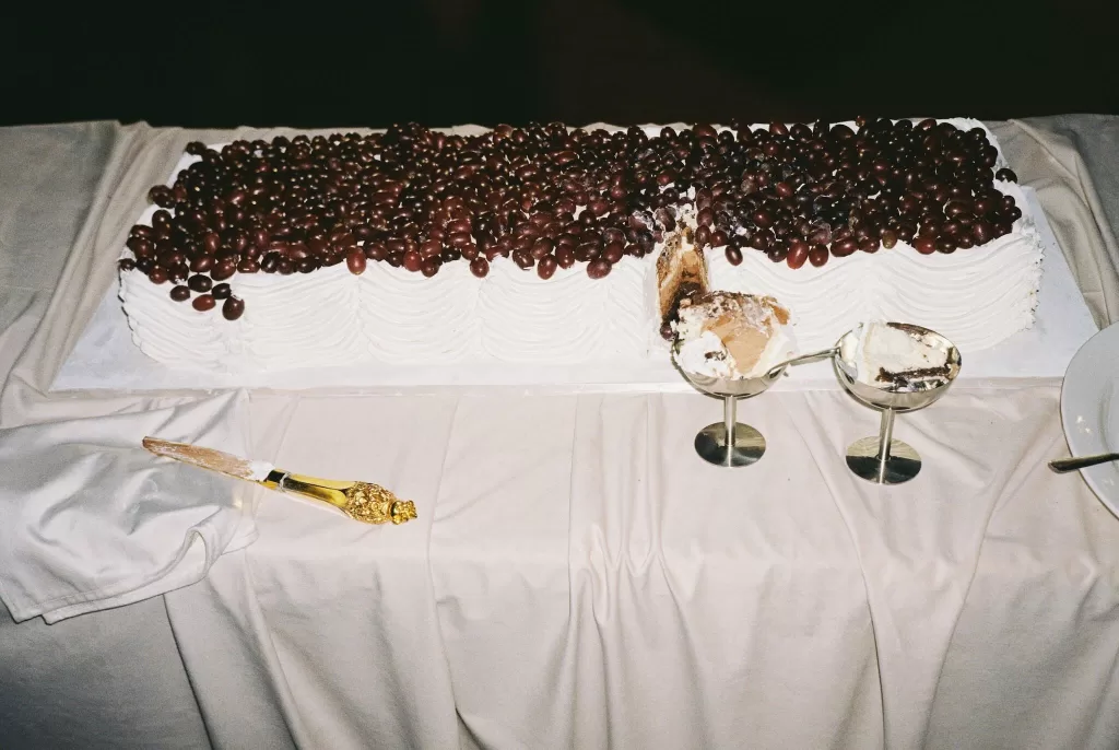 Rectangular wedding cake topped with fresh grapes, partially sliced and displayed on a cream tablecloth.