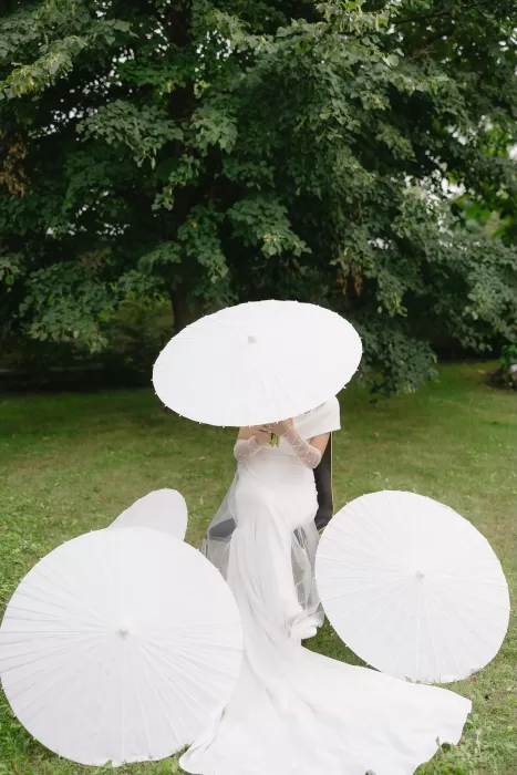 Bride seated in the grass surrounded by white parasols at Winery Hans Igler.