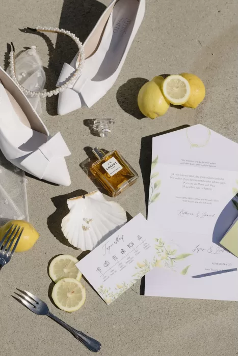 Flatlay of wedding day details including white heels, pearl headband, Chanel perfume, and lemons at Winery Hans Igler.
