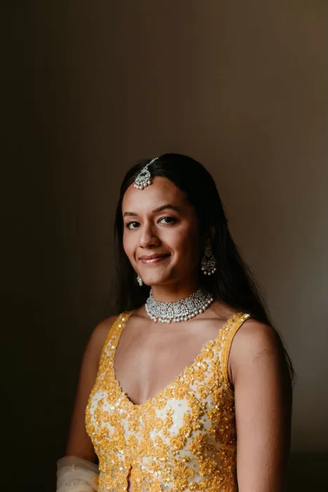 Bride in intricately embroidered yellow lehenga and statement jewellery, smiling softly before the ceremony.