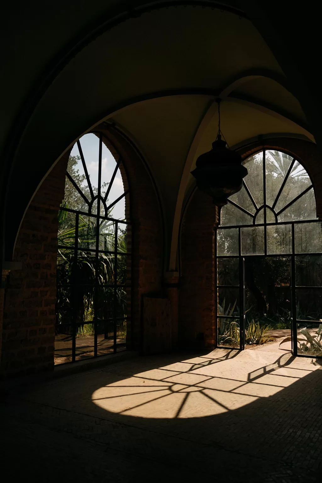 Sunlight streaming through arched windows, casting patterned shadows on the stone floor at Beldi Country Club.