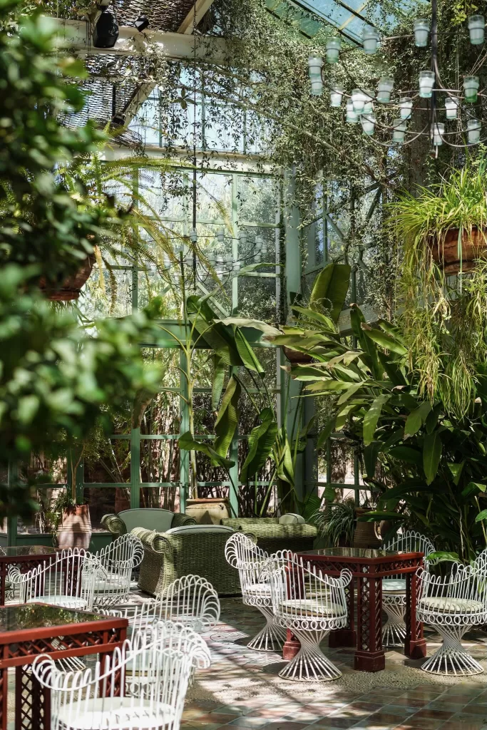 Elegant greenhouse seating at Beldi Country Club surrounded by tropical plants and natural light.