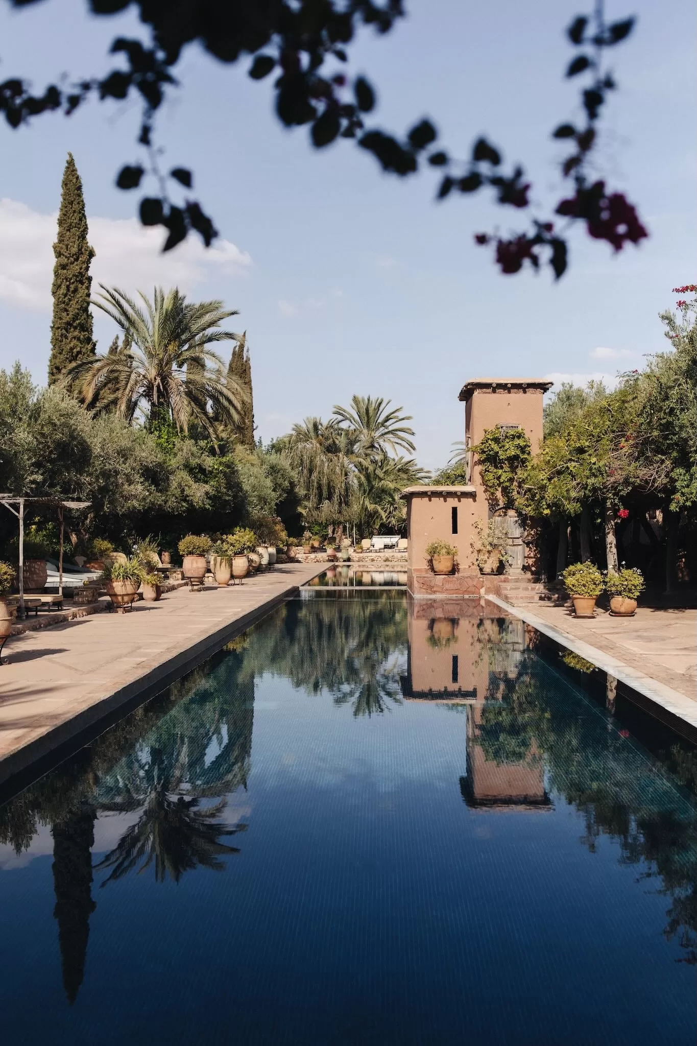 Long reflective pool surrounded by palms and terracotta walls at Beldi Country Club, capturing a serene Mediterranean atmosphere.