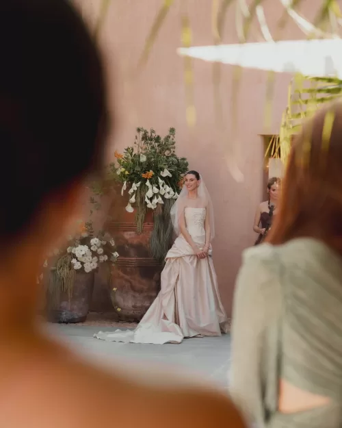 Bride in strapless gown and veil standing before floral ceremony backdrop.