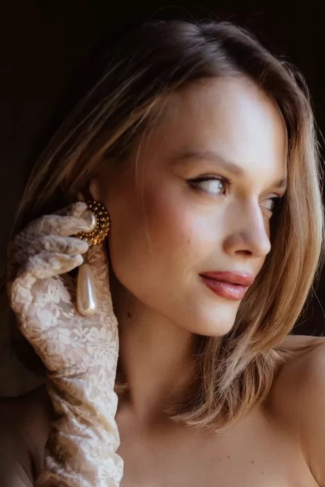 Bride wearing statement pearl earrings and lace gloves in soft light at Chateau Challain.