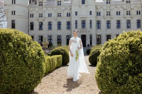 Bride in flowing gown holding bouquet while walking through manicured gardens at Chateau Challain.