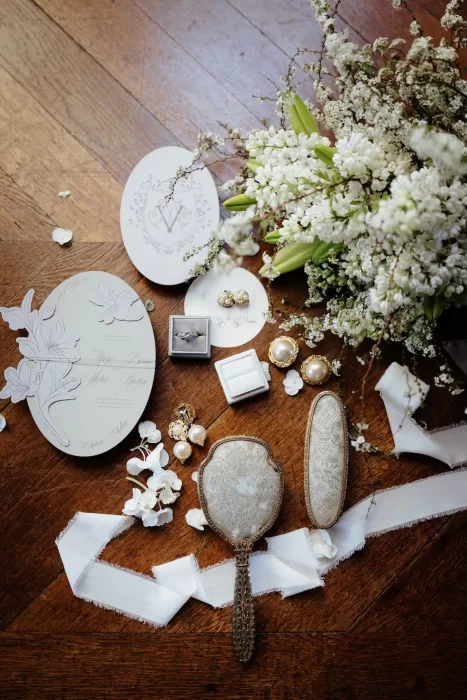 Elegant flat lay of wedding invitations, jewelry, and florals on wooden floor at Chateau Challain.