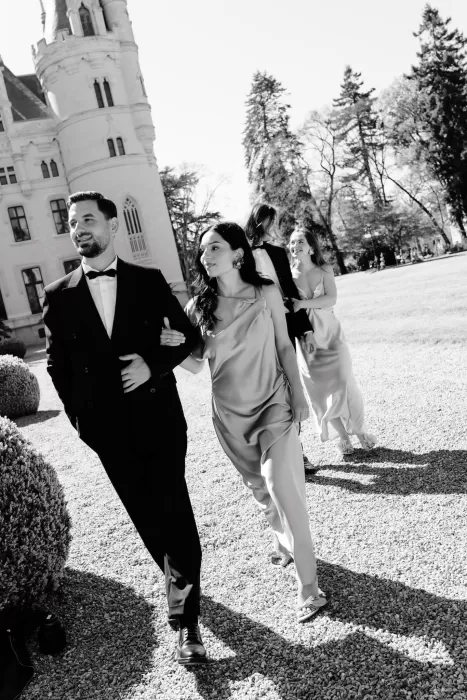 Stylish wedding guests walking arm in arm through the gardens of Chateau Challain.