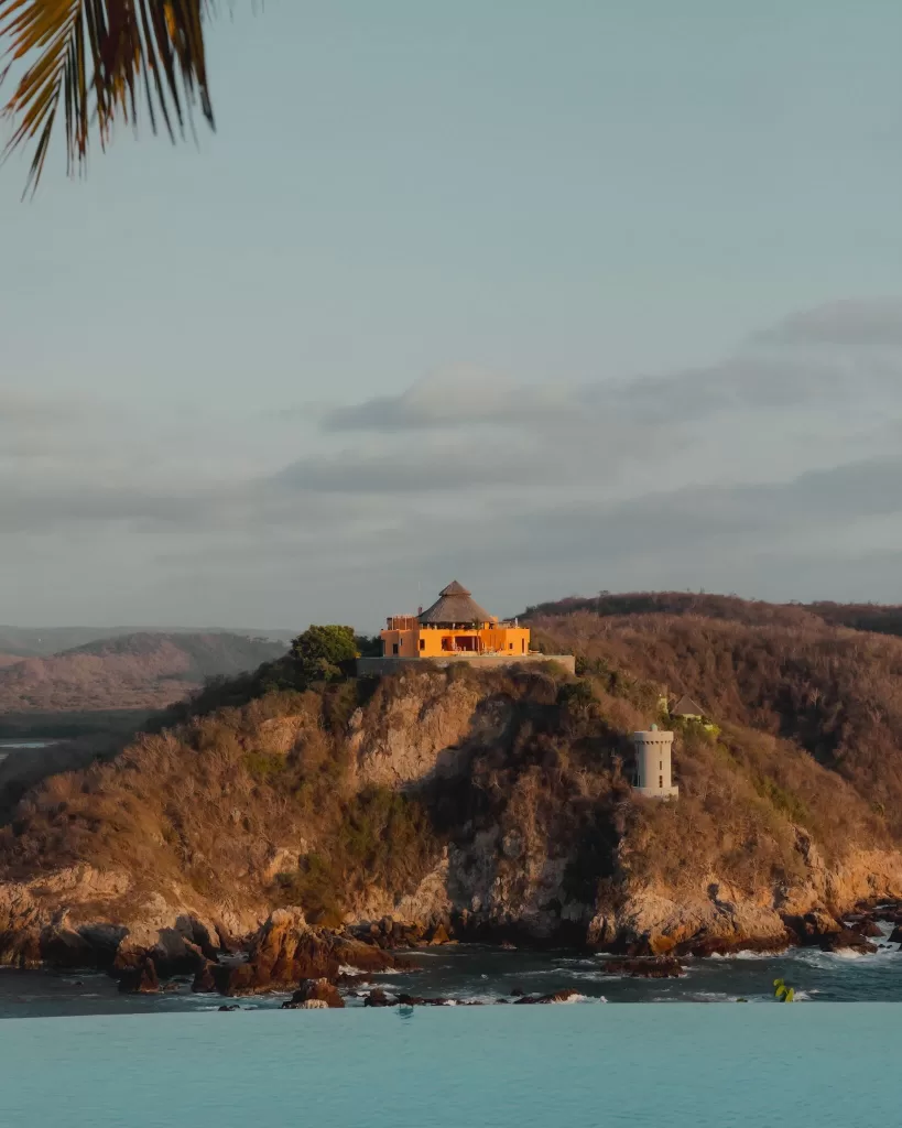 Striking view of a yellow villa perched on a cliff above the ocean at sunset.