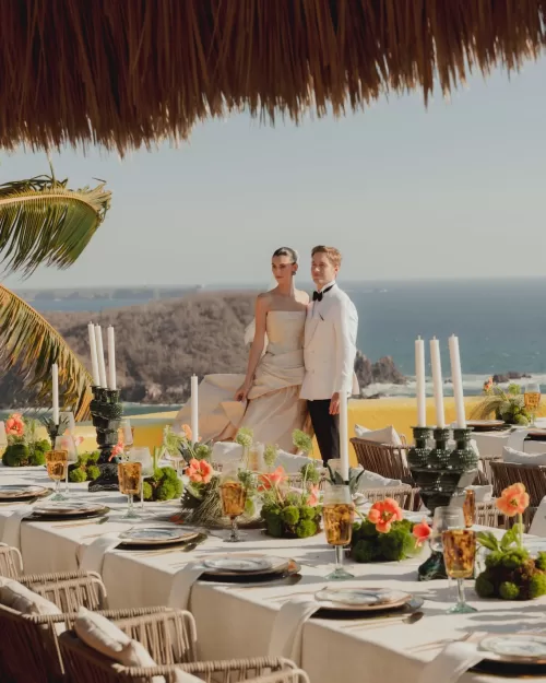 Bride and groom standing on a terrace with ocean views and floral wedding table décor.