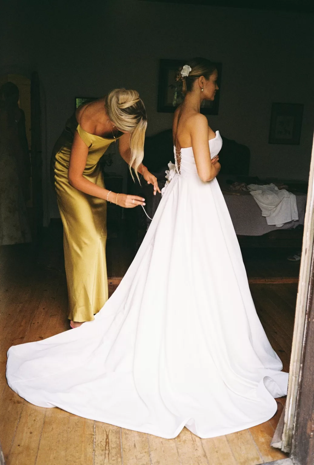 Bridesmaid helping bride lace up her elegant wedding gown before the ceremony, captured by Domrose Photography.