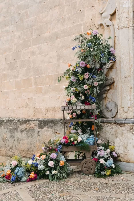 Overflowing floral cart with colourful blooms against the church wall at Finca Son Collell