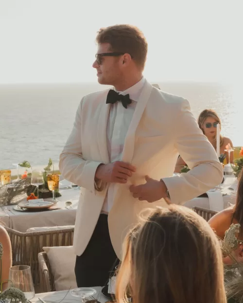 Groom in a white tuxedo jacket and black bow tie at the seaside reception.