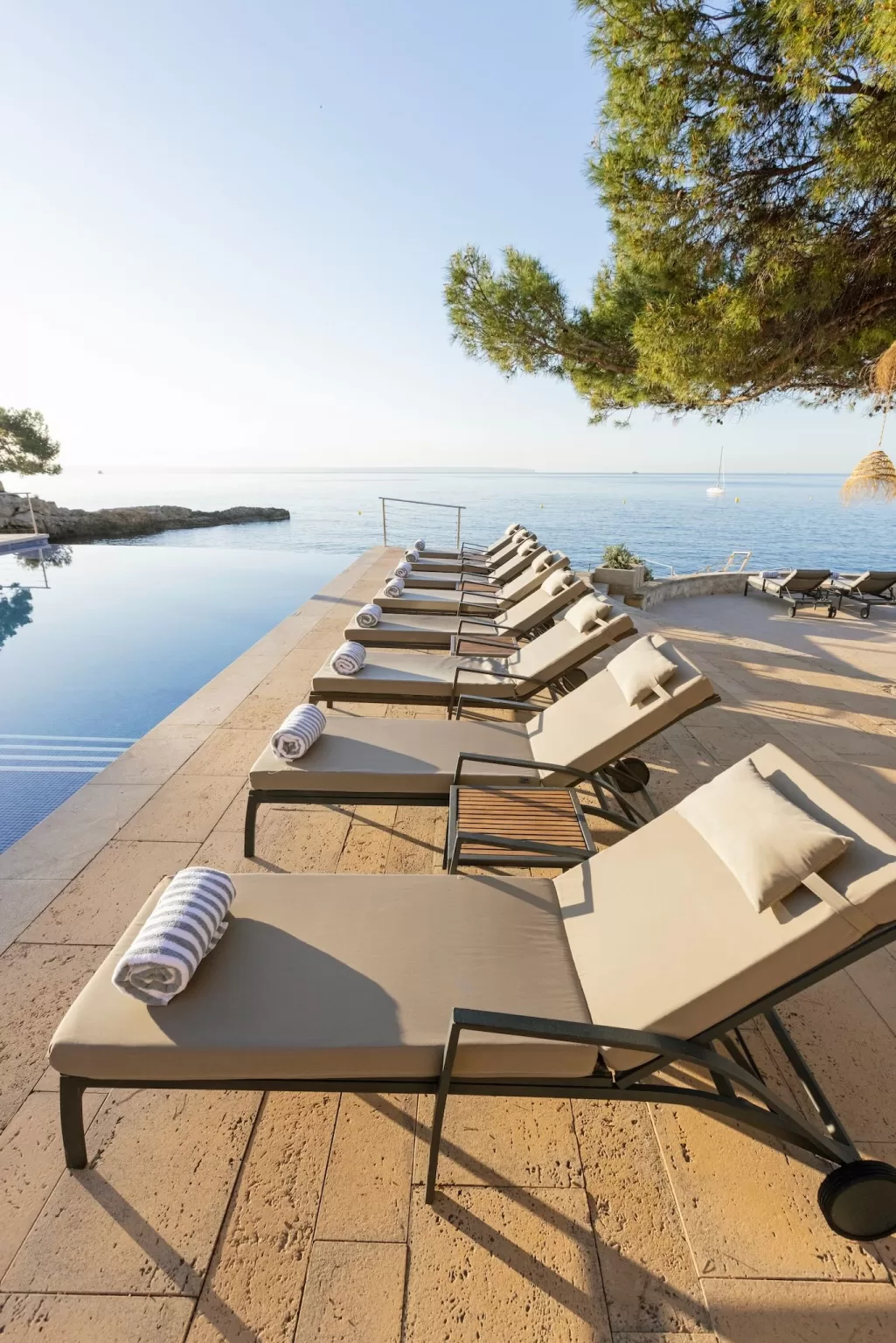 Infinity pool loungers at Hospes Maricel lined up beside the sea at sunrise.