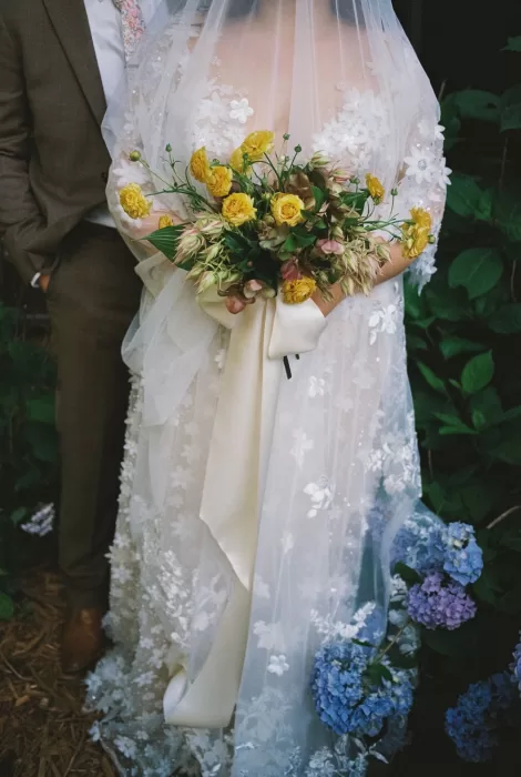 Detailed shot of bride’s bouquet with yellow roses and blush florals held against her lace dress at House Boheme.