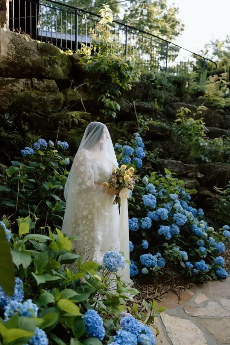 Bride in a long veil holding a bouquet surrounded by vibrant hydrangea blooms at House Boheme.