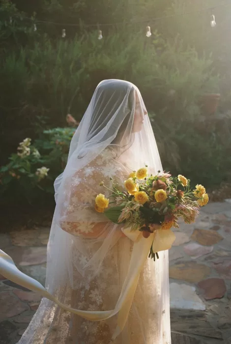 Bride with veil and bouquet of yellow roses bathed in warm golden sunset light at House Boheme.