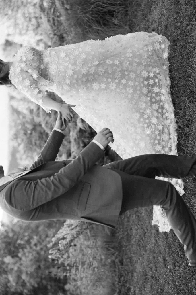 Bride and groom share a tender handhold outdoors, her floral lace gown flowing elegantly at House Boheme.