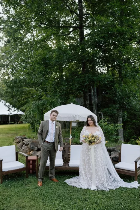 Wedding couple pose together on the lawn with white lounge seating and greenery at House Boheme.