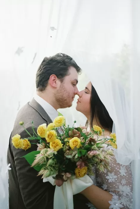 Bride and groom kiss softly beneath the veil with a golden rose bouquet at House Boheme.