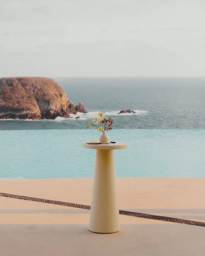 Minimalist pedestal table with floral arrangement beside infinity pool and sea views.
