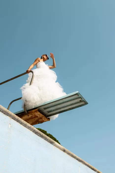 Bride in a voluminous gown standing on a diving board against a clear blue sky at La Finka 4.1.