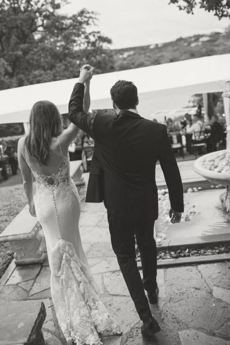 Newlyweds raising their hands in celebration while walking together at Laguna Gloria.