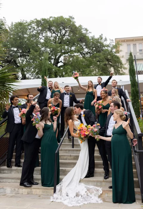 Wedding party cheering around the couple kissing on the stairs at Laguna Gloria.