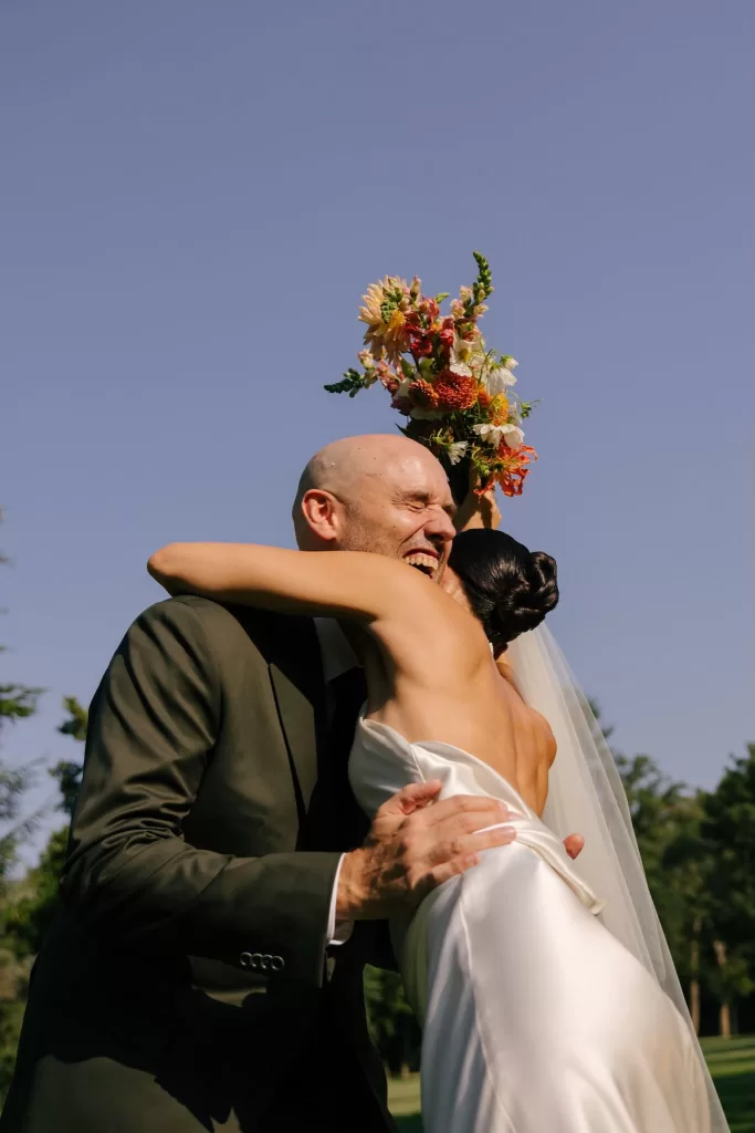 Groom embracing bride lifting bouquet in the air during joyful outdoor celebration, captured by Lucky Elevens.