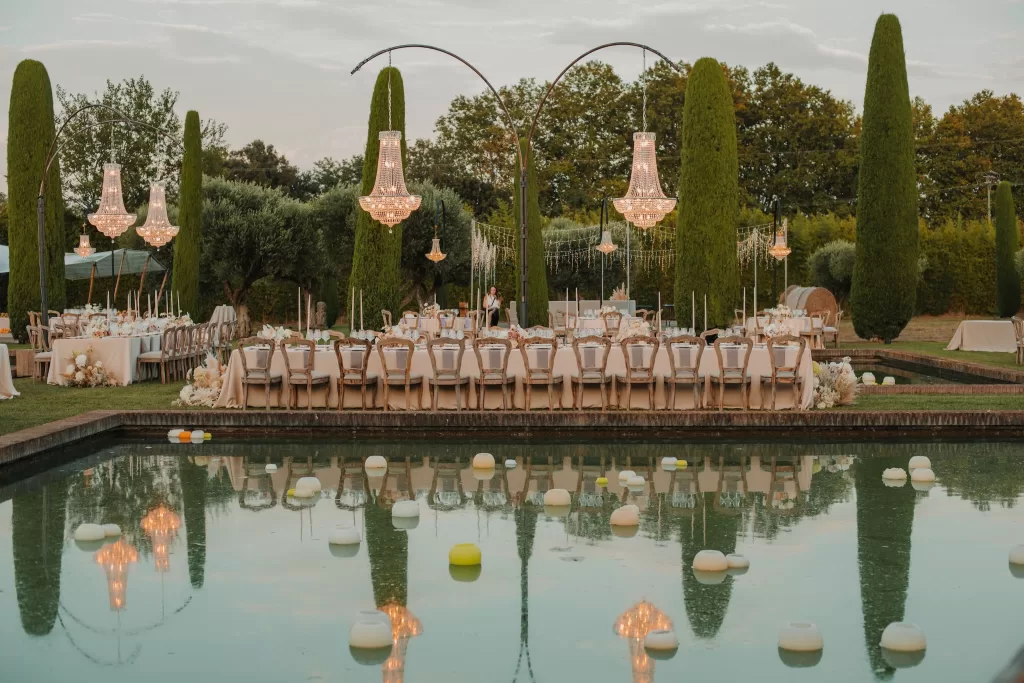 Elegant poolside dining tables with chandeliers at Mas de Les Voltes wedding.