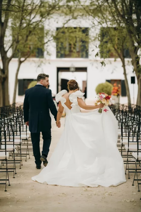 Newlyweds walking down the aisle together with bride’s flowing gown at Masia Aldamar.