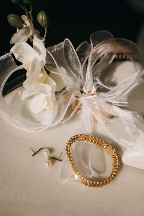 Elegant wedding accessories including gold bracelet, pearl earrings, and ribbon-wrapped rings at Masia Aldamar.