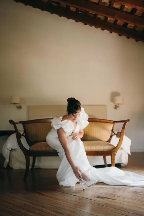 Bride putting on shoes in a rustic room with wooden floors at Masia Aldamar.