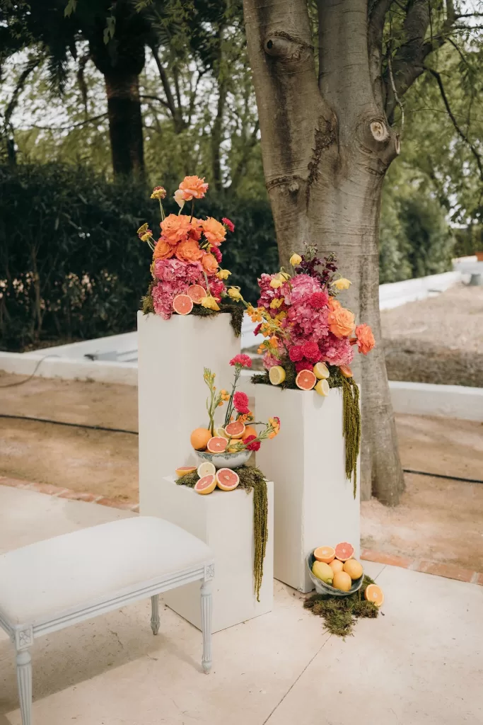 Vibrant floral arrangements with citrus fruit details adorning outdoor ceremony space at Masia Aldamar.