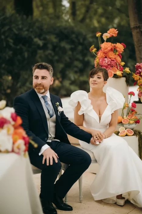 Bride and groom seated hand in hand during outdoor ceremony at Masia Aldamar.
