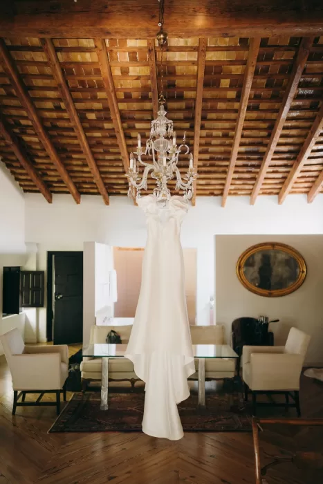 Wedding gown with sculptural sleeves hanging from chandelier in rustic suite at Masia Aldamar