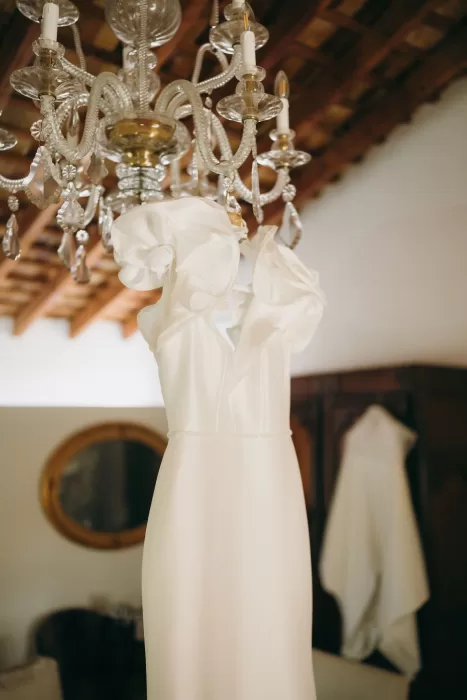 Elegant wedding gown with floral sleeves hanging from chandelier at Masia Aldamar.