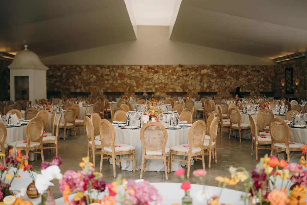 Elegant reception hall at Masia Aldamar decorated with round tables and colorful floral centerpieces.