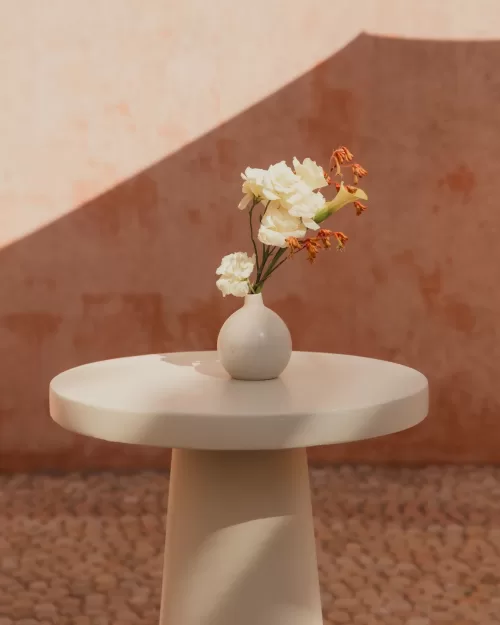 Simple white vase with fresh flowers on a round table against textured peach walls.