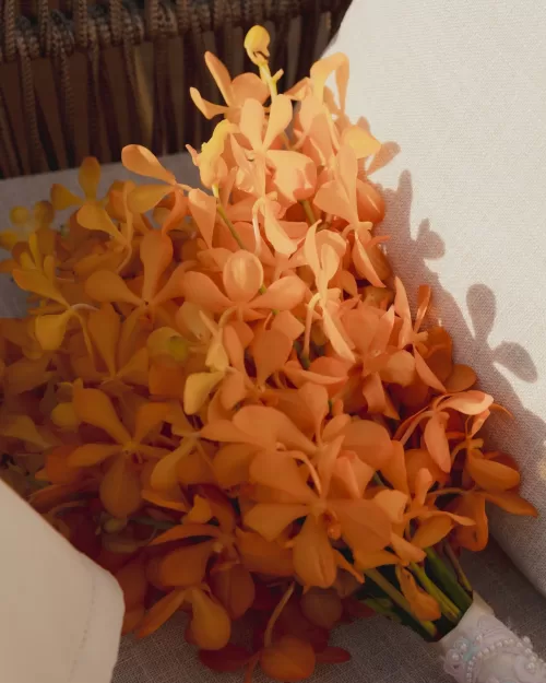 Close-up of a vibrant orange wedding bouquet resting on a chair.
