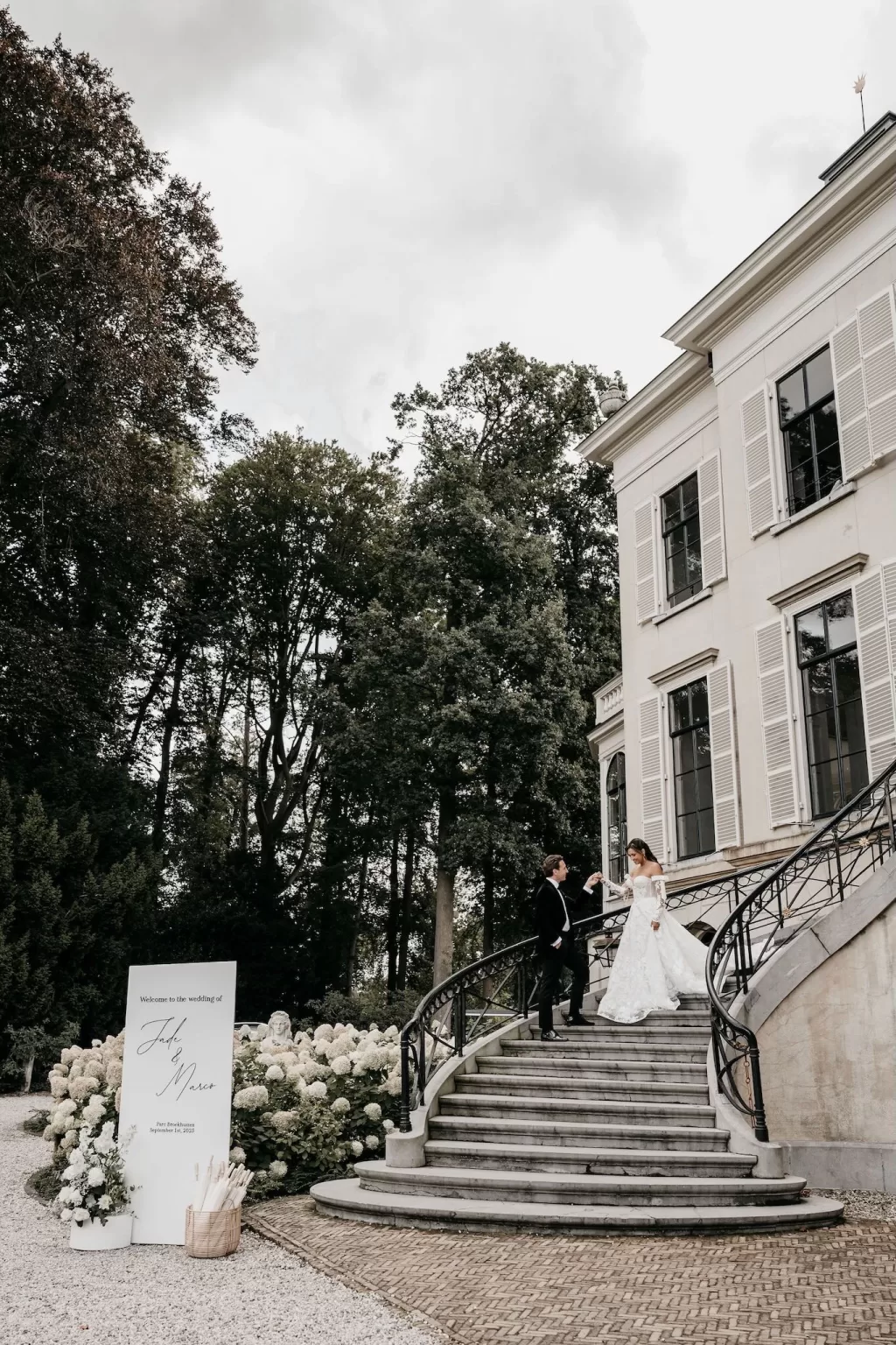 Groom helping bride descend the sweeping staircase of Parc Broekhuizen.