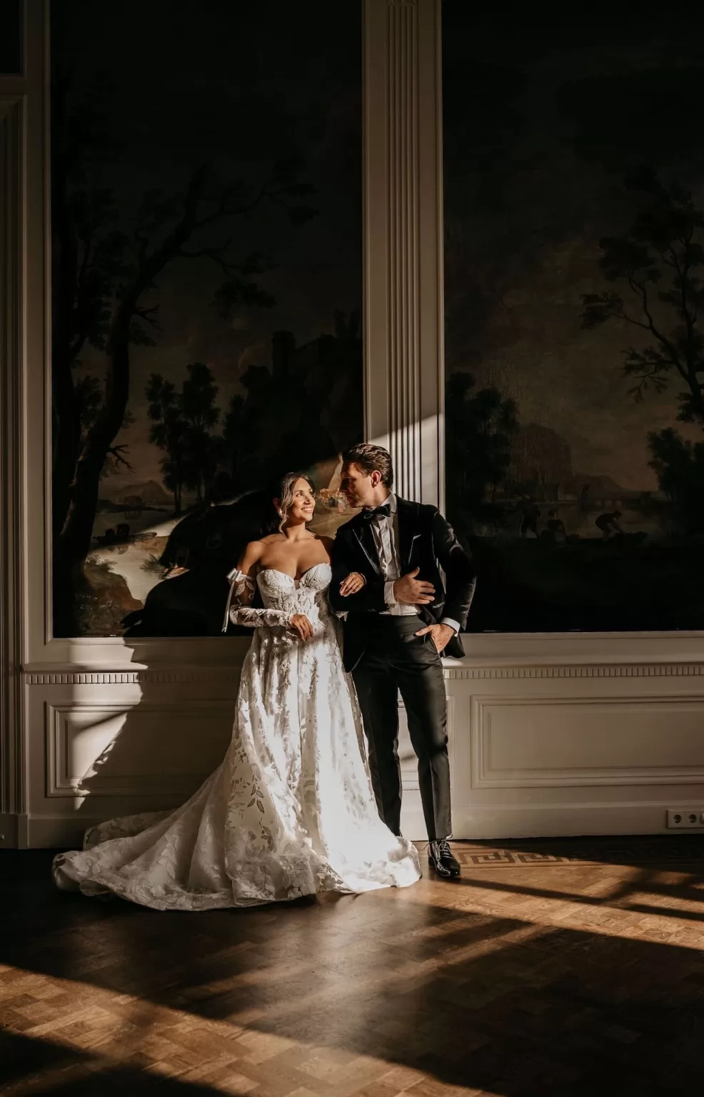 Bride and groom in elegant wedding attire standing in a sunlit room at Parc Broekhuizen.